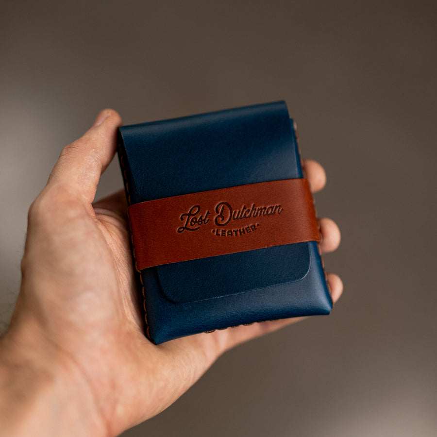 Hand holding a navy leather wallet with a brown wrap band
