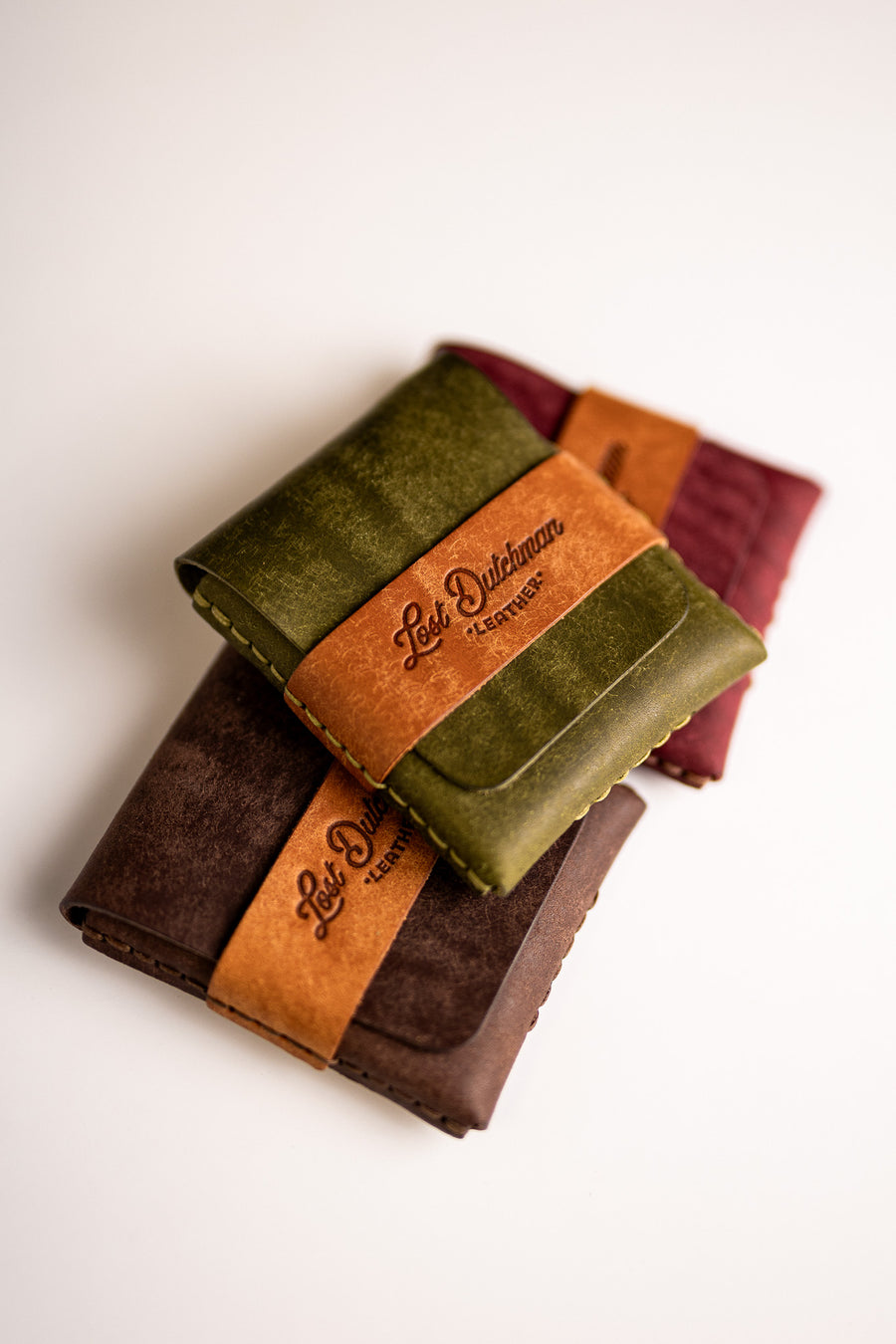 Stack of olive green, burgundy and brown leather wallets with tan wrap bands