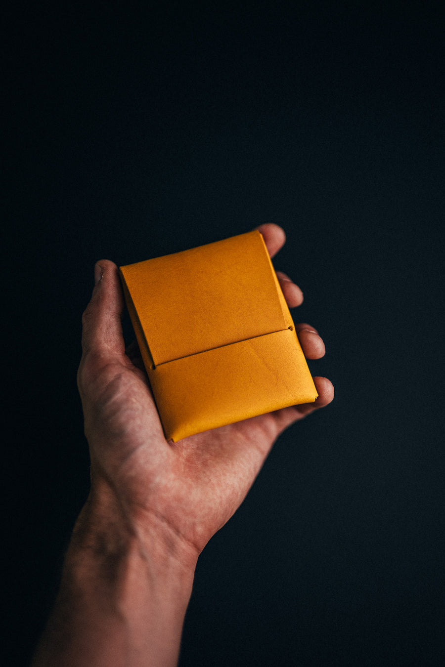 Hand holding a mustard-yellow leather wallet against a dark background
