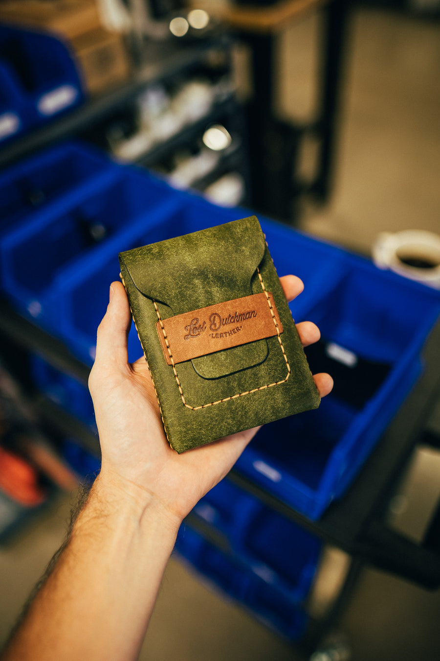 Hand holding an olive green leather wallet in a workshop