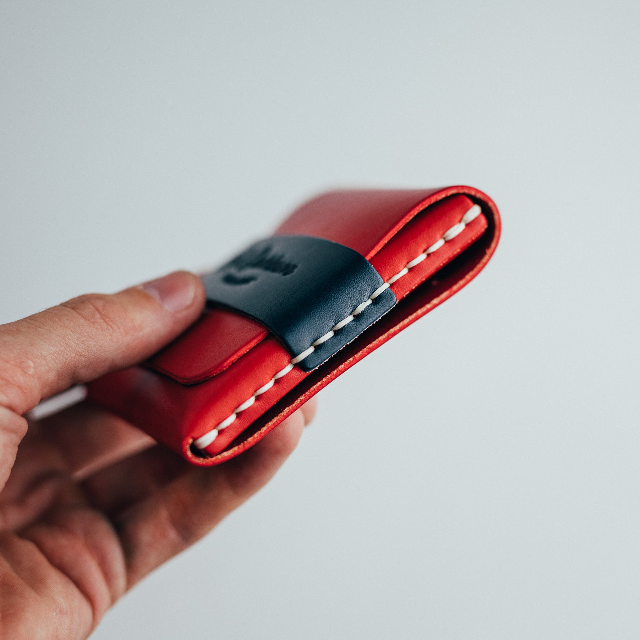 Hand holding a red leather wallet with a dark wraparound band