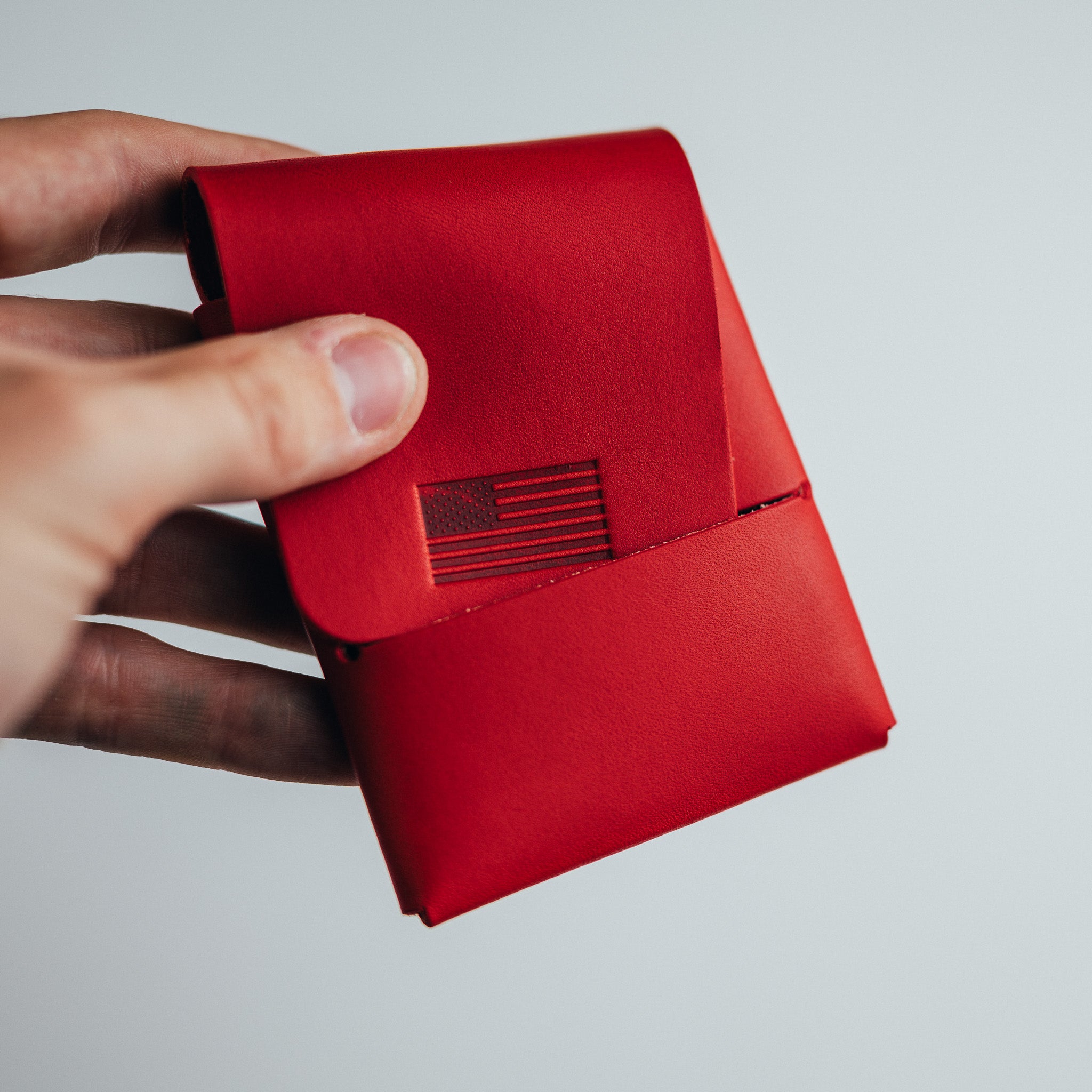 Hand holding a red leather wallet with a small embossed flag