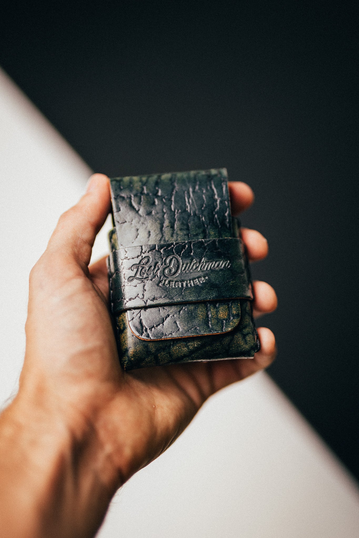 Hand holding a dark patterned leather wallet