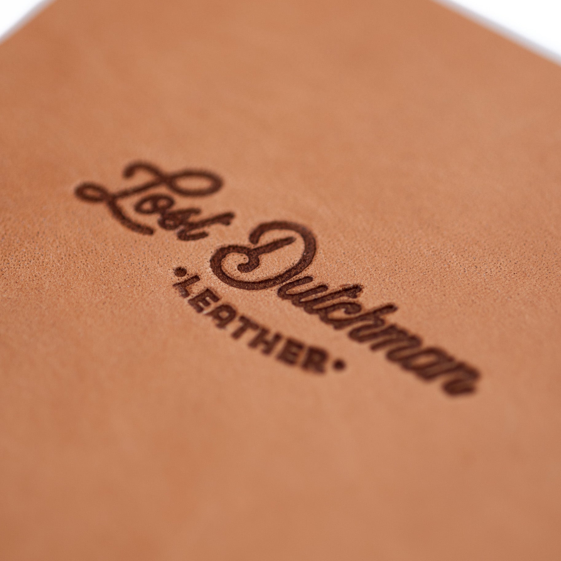 Close-up of a leather coaster with 'Lost Dutchman Leather' embossed on it.
