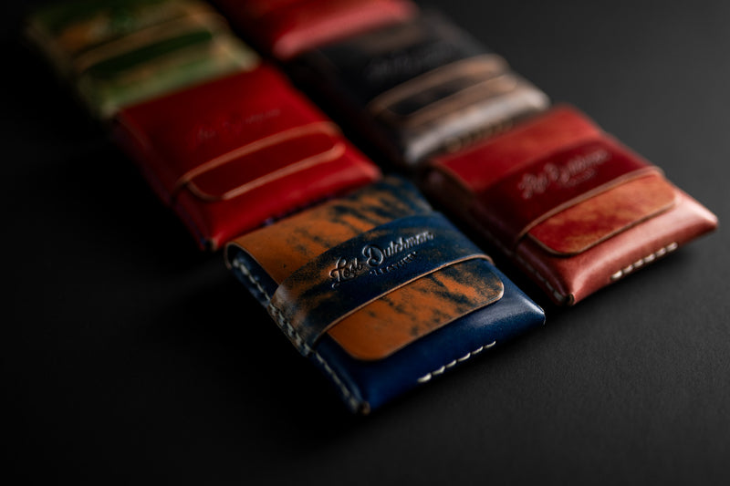 Stack of red, brown and blue leather card holders on a dark surface