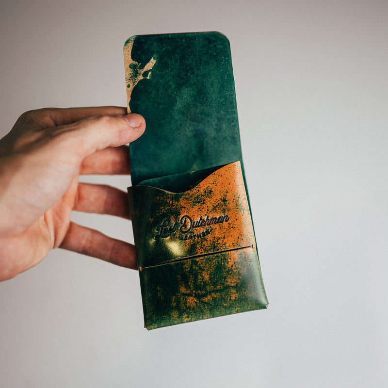 Hand holding a dark teal and patterned brown leather card holder