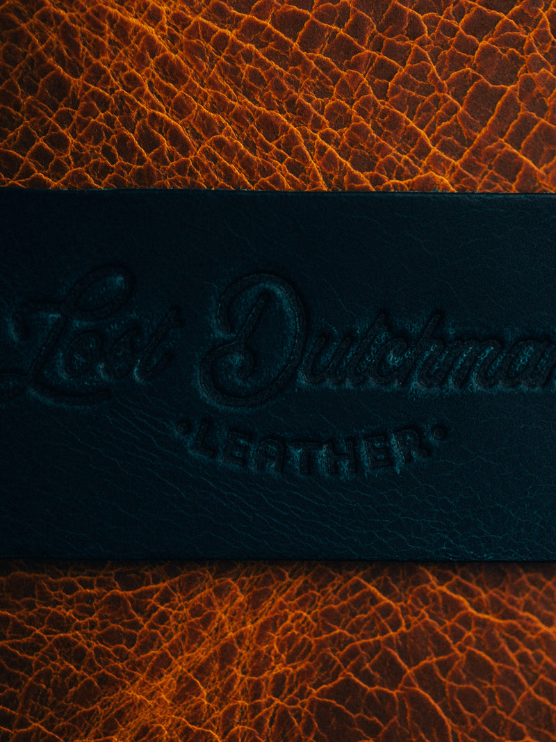 Close-up of embossed Lost Dutchman Leather logo on dark teal and brown leather