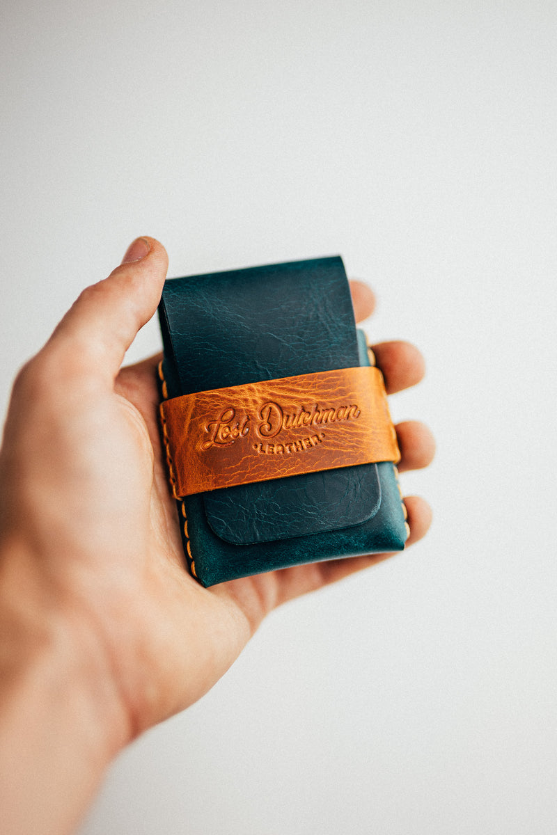 Hand holding a dark teal and brown leather card holder