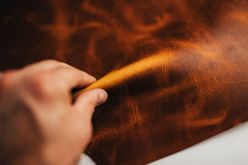 Hand pinching and lifting a fold in brown leather