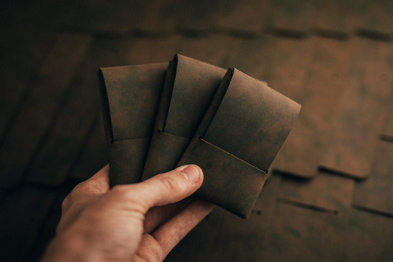 Hand holding several dark leather wallet sleeves