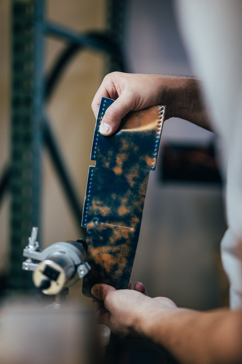 Hand holding a dark patterned leather wallet beside a bicycle
