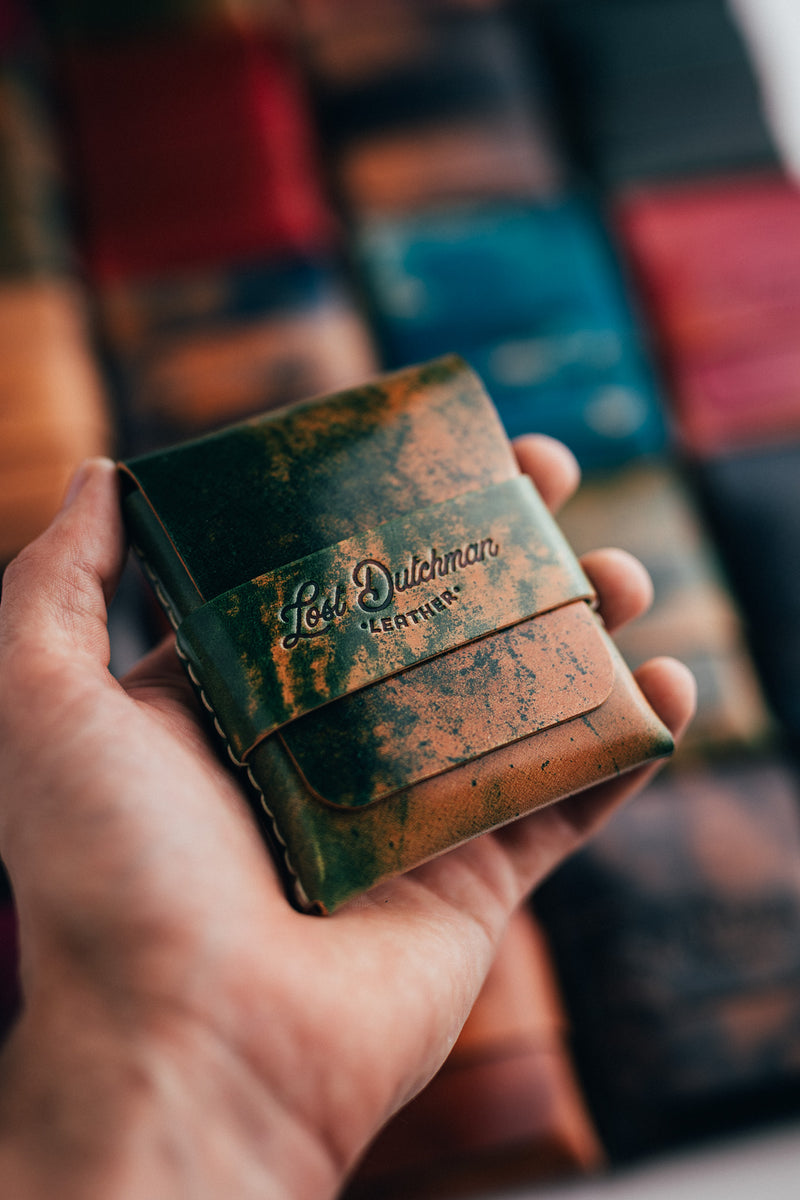 Hand holding a green and brown patterned leather wallet