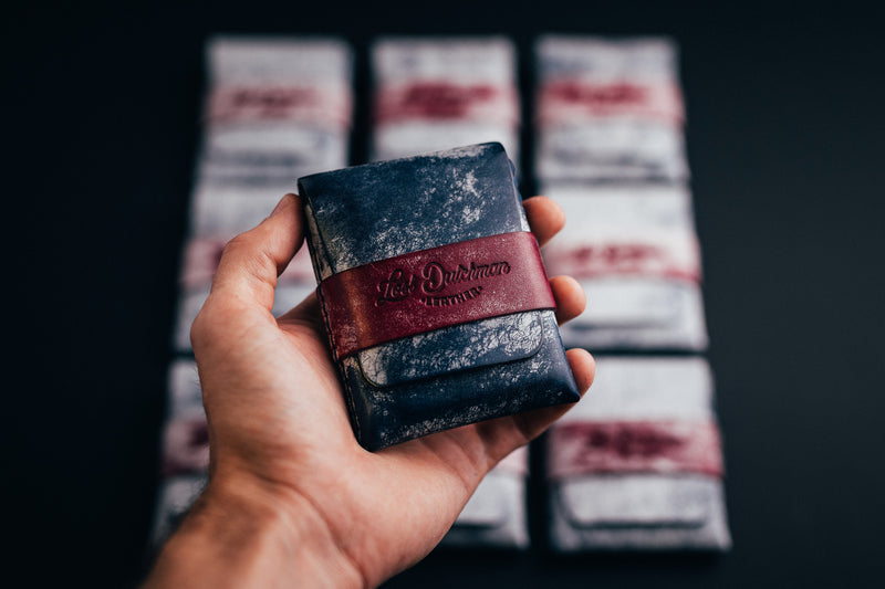 Hand holding a patterned dark leather wallet with a burgundy band
