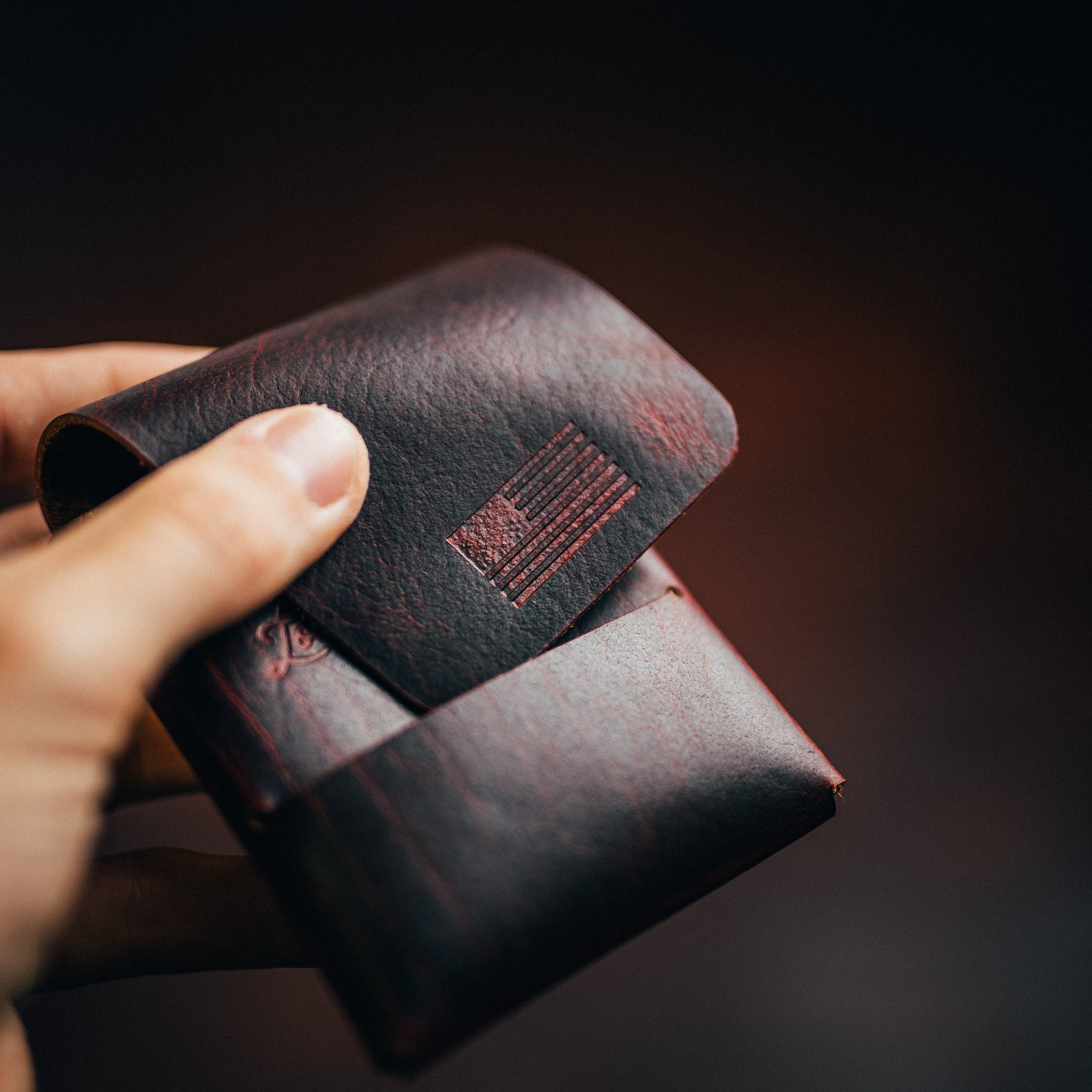Hand holding a dark leather wallet with a small embossed flag