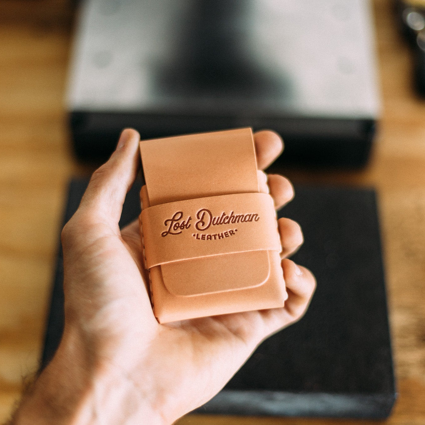 Hand holding a tan "Lost Dutchman Leather" handmade leather wallet.