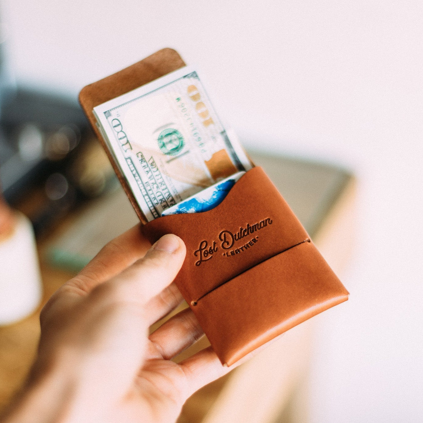 Hand holding a brown leather "Lost Dutchman" wallet with cash and a card inside.